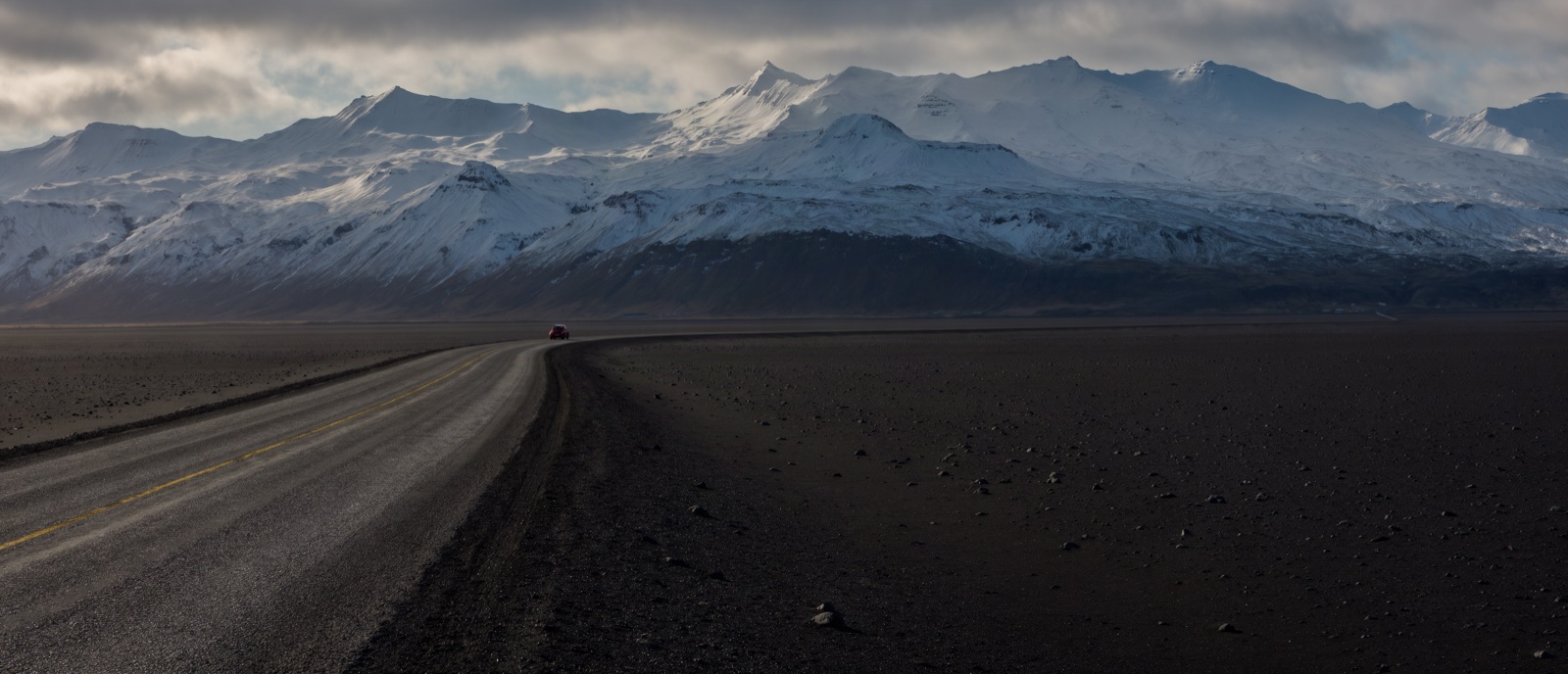 Empty road through black volcanic sand toward snow-capped mountains in Iceland, Krea 3